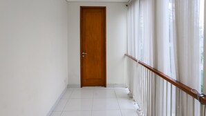 A corridor with a wooden door, white tiled floor, and a white railing with a wooden handrail. - OYO 93370 Lot Thirty Six (Bekasi)