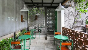 A café with green tables and chairs, a concrete wall with art, and a wooden fence with plants. - OYO 93370 Lot Thirty Six (Bekasi)