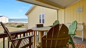 Una habitación con una mesa y sillas de madera, una ventana con vista a la playa y un cartel en la pared.