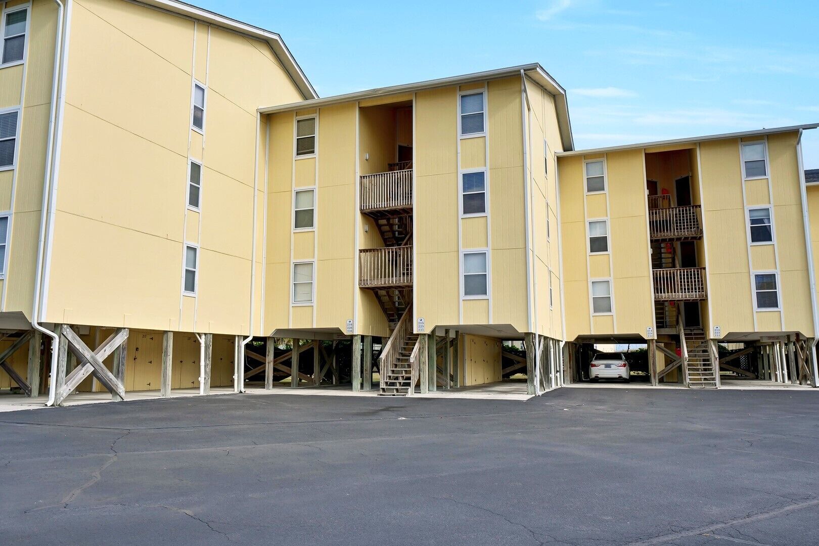 A multi-story yellow building with external staircases and a parking area in front.