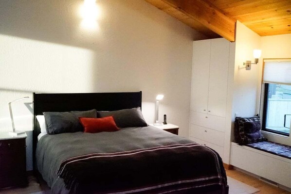 Un dormitorio con cama, mesitas de noche, ventana y espacio de almacenamiento integrado.