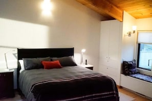 A bedroom with a bed, bedside tables, a window, and built-in storage. - Oasis | Ocean Views & Private Hot Tub (Sea Ranch)