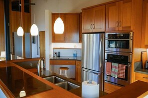 A kitchen with wooden cabinets, stainless steel appliances, a double sink, and pendant lighting. - Oasis | Ocean Views & Private Hot Tub (Sea Ranch)
