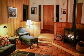 Una sala acogedora con chimenea, un sofá, un sillón y una lámpara.