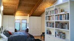 A bedroom with a large bed, a bookshelf, and a window. - Oasis | Ocean Views & Private Hot Tub (Sea Ranch)