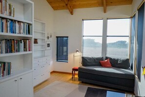 A room with a bookshelf, a sofa, a window, and a lamp.
