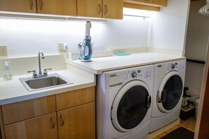 A compact laundry area with a sink, two washing machines, and wooden cabinets.