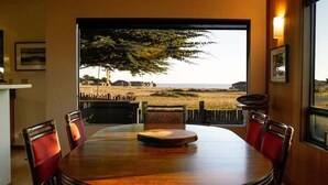 A dining area with a round table and chairs, a view of the outdoors, and a large window. - Oasis | Ocean Views & Private Hot Tub (Sea Ranch)