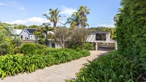 A modern house with a paved pathway, surrounded by lush greenery and palm trees. - 6 BEDROOM FAMILIES SENSATION, LARGE HOLIDAY BEACH ENTERTAINER IN PORTSEA (Portsea)