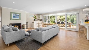 A modern living room with a fireplace, grey sofas, and a dining area with natural light. - 6 BEDROOM FAMILIES SENSATION, LARGE HOLIDAY BEACH ENTERTAINER IN PORTSEA (Portsea)