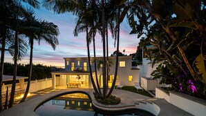 Une maison moderne avec une piscine, entourée de palmiers et offrant une vue imprenable sur le coucher de soleil.