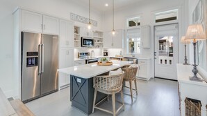 A modern kitchen with white cabinetry, stainless steel appliances, and a central island with bar stools.