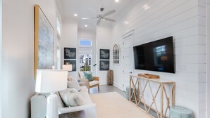 A modern living room with a large flat-screen TV, white walls, and a ceiling fan.