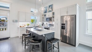 Una cocina moderna con armarios blancos, electrodomésticos de acero inoxidable y una isla central con taburetes de bar.