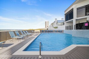 Une piscine avec des chaises longues, une terrasse et un bâtiment sur lequel est affiché un panneau indiquant qu’il est interdit de plonger.