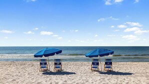 Uma praia com dois guarda-sóis azuis e duas cadeiras de praia viradas para o oceano.