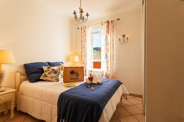 Un lit bien fait, avec une couverture bleue, un coussin à motifs floraux et une plaque en bois sur laquelle on peut lire « PROVENCE ».
