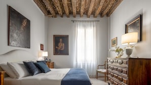 A bedroom with a wooden ceiling, a bed with pillows, a dresser, and a window with curtains. - Miracoli Apartment with View on the Canal R&R (Venecia)