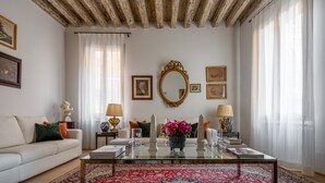 A living room with a wooden ceiling, a glass coffee table, a white sofa, and a large mirror. - Miracoli Apartment with View on the Canal R&R (Venecia)