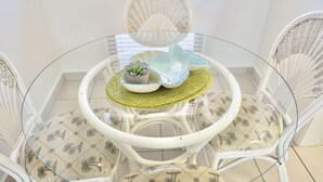 A round glass table with a woven placemat, surrounded by white wicker chairs with patterned cushions.