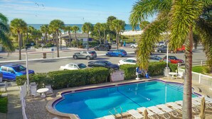 A swimming pool with lounge chairs and umbrellas, surrounded by palm trees and a view of the beach.