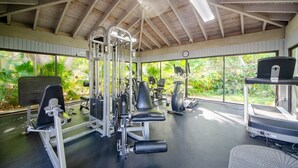 A gym with various exercise equipment, large windows, and a wooden ceiling.