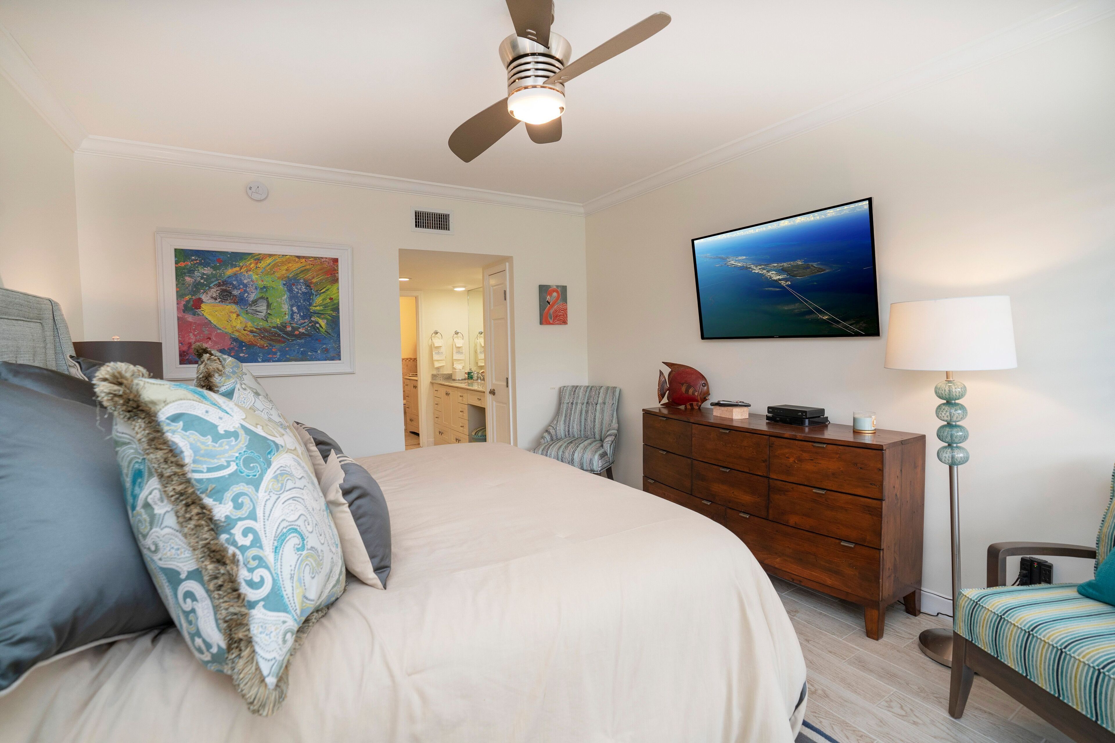 Ein Schlafzimmer mit Bett, Deckenventilator, Kommode, Stuhl und Bildern an den Wänden.