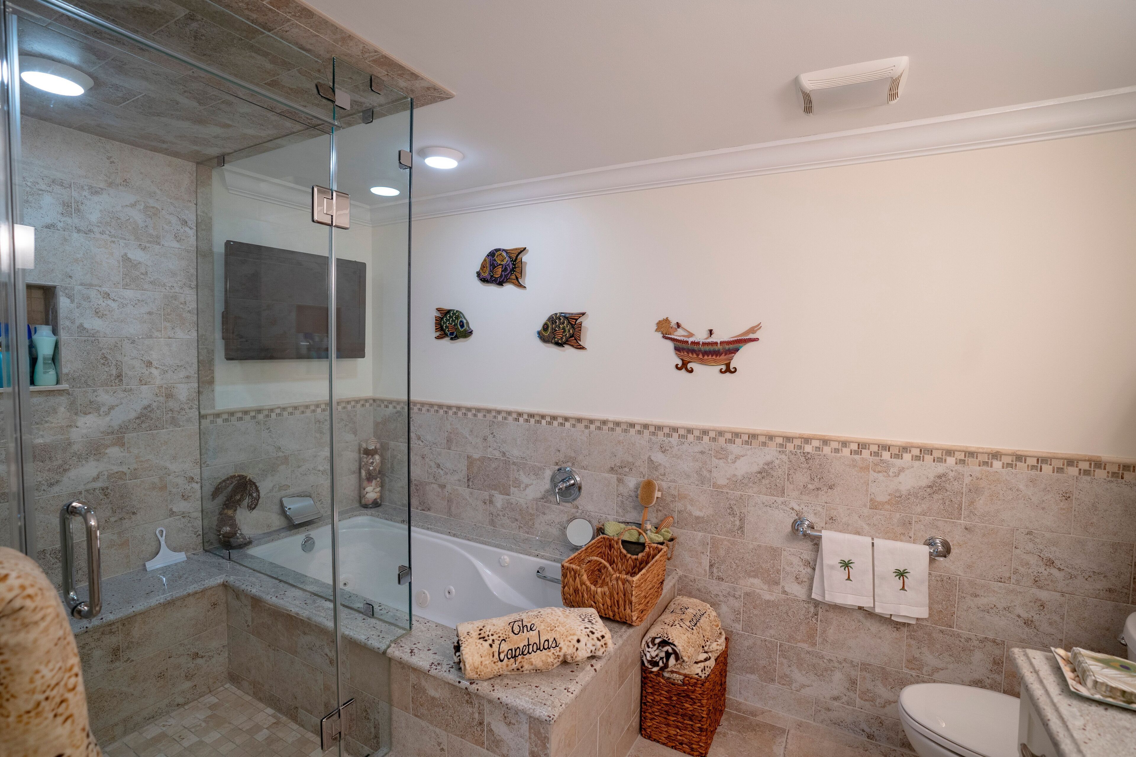 A bathroom with a glass shower enclosure, a bathtub, and a toilet. There are decorative wall tiles and a small shelf with toiletries.