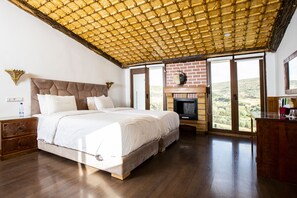 Un'ampia camera da letto con un grande letto, pavimento in legno, camino in mattoni e vista sull'esterno.