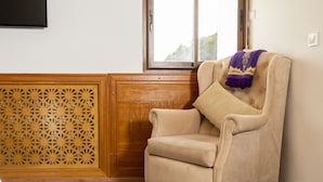 Un fauteuil beige, agrémenté d’un coussin et recouvert d’un plaid violet, est placé à côté d’un panneau en bois orné de motifs complexes découpés.