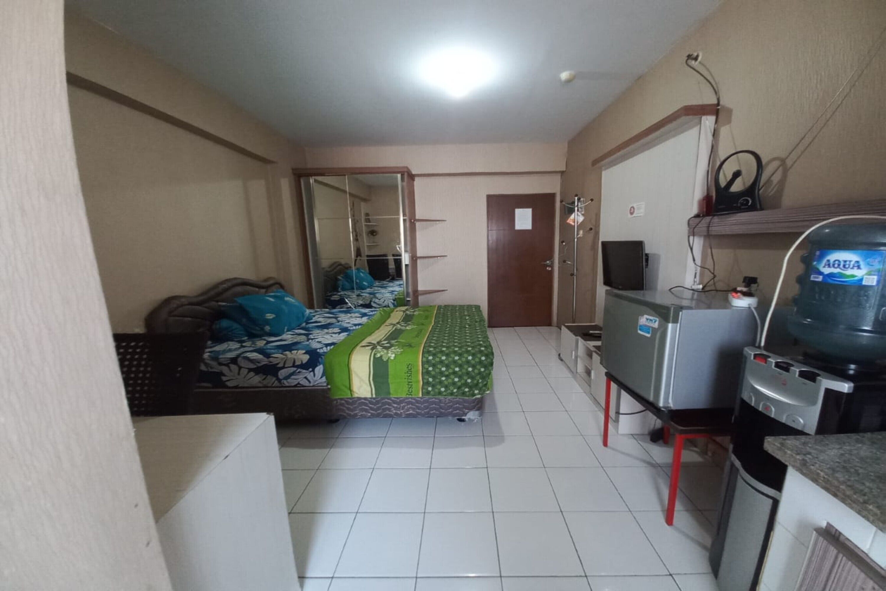 A bedroom with a bed, a small kitchenette, a water dispenser, and a door leading to another room.