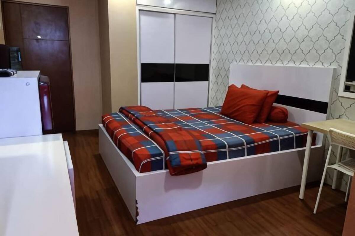 Una cama con cabecera, una mesita de noche, un armario y un escritorio.