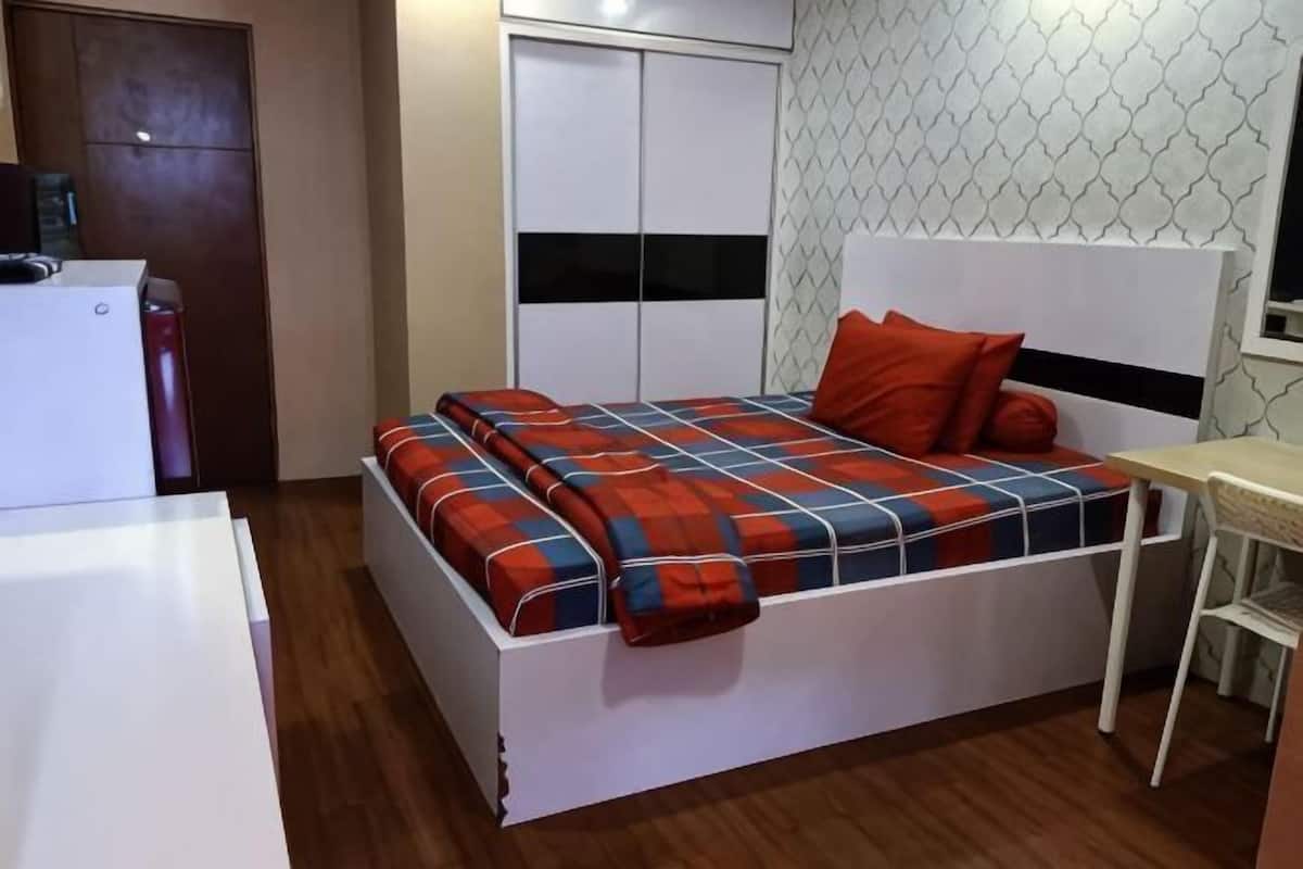 A bed with a headboard, a bedside table, a wardrobe, and a desk.