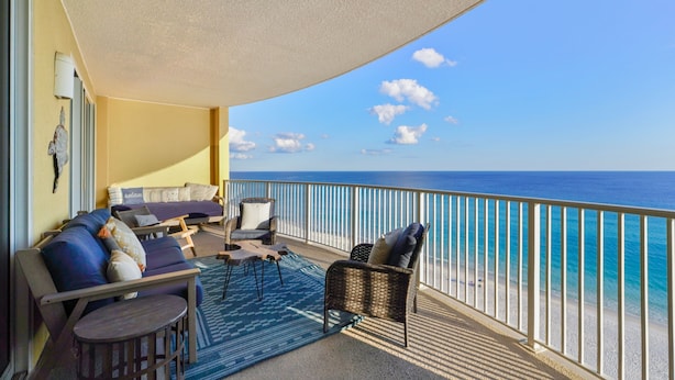 A balcony with a sofa, chairs, and a small table, overlooking a beach.