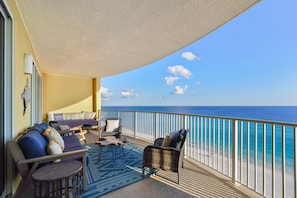 A balcony with a sofa, chairs, and a small table, overlooking a beach.