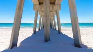 A concrete pier structure extending into a sandy beach with clear blue water.