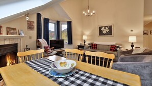 Un salón acogedor con chimenea, una mesa de comedor con mantel a cuadros y una televisión.