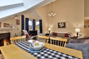 Un salón acogedor con chimenea, una mesa de comedor con mantel a cuadros y una televisión.