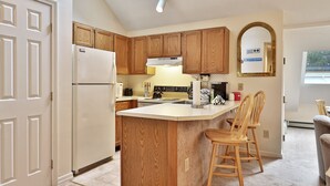 Una cocina con armarios de madera, un refrigerador blanco, una isla integrada con taburetes de bar y una ventana con vistas.