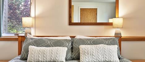 A neatly made bed with a patterned bedspread and two decorative pillows, a wooden headboard, and a mirror with a wooden frame on the wall.