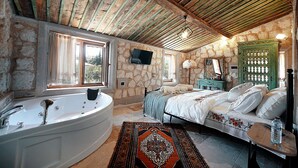 Ein rustikales Schlafzimmer mit Stewand, einer großzügigen Badewanne, einem Bett mit gemustertem Überwurf und einer Holzbalkendecke.