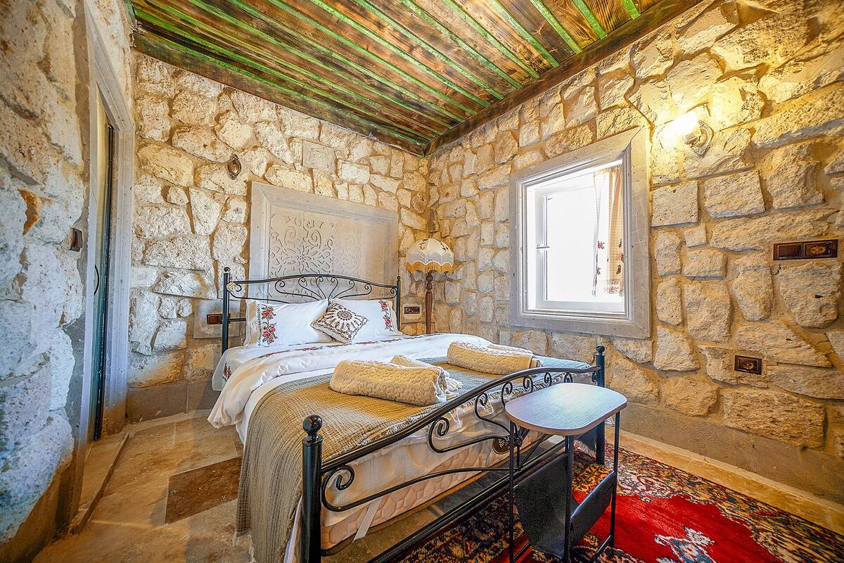 Une pièce aux murs de pierre, avec un lit, une petite table et une fenêtre.