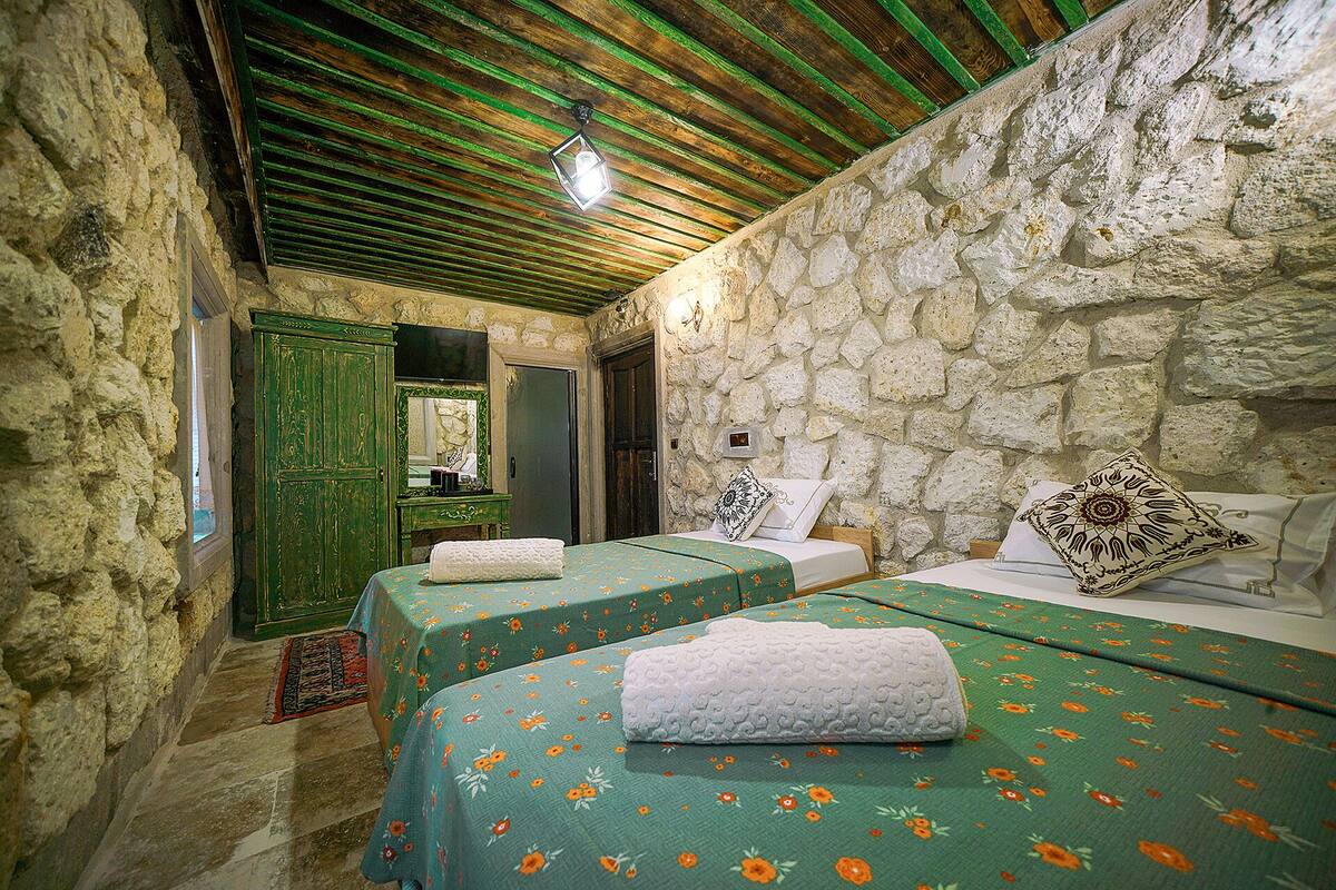 Une chambre avec deux lits, des murs en pierre, un plafond en bois et une porte verte.