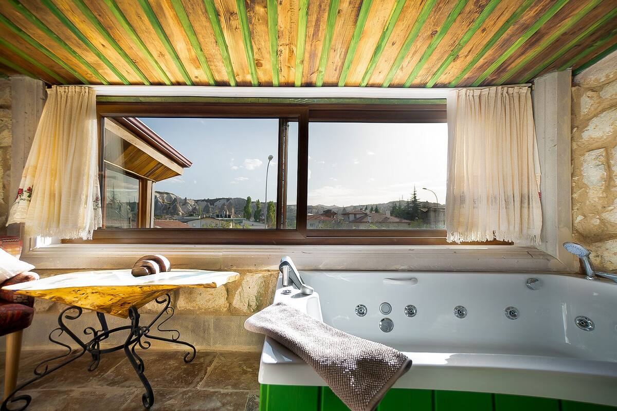 Une salle de bain avec une baignoire, une fenêtre avec des rideaux et une vue sur l’extérieur.