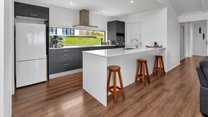 A modern kitchen with a large island, wooden stools, and a view of the outdoors. - Seaglass - Karikari Peninsula Holiday Home (Kaitaia)