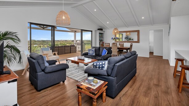 A spacious living area with a large window, a sofa set, a coffee table, and a dining area. - Seaglass - Karikari Peninsula Holiday Home (Kaitaia)