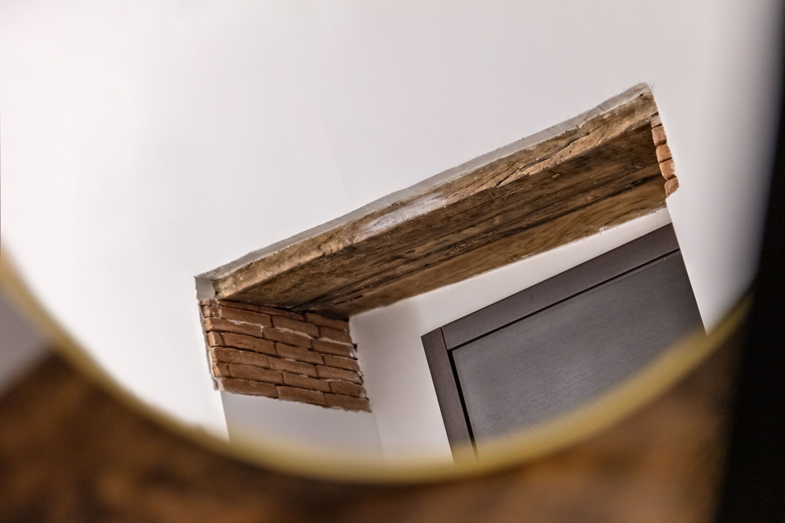 A close-up of a wooden beam above a door, with a brick wall partially visible.