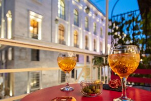 A table with two glasses of amber liquid, a small bowl of pickles, and a slice of pizza on a red table in an outdoor setting with a building in the background. - Residenza Toledo Lifestyle (Naples)