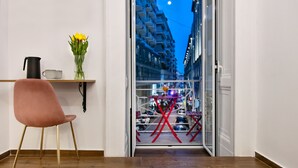 A room with a wooden floor, a pink chair, a black pitcher, a glass vase with yellow flowers, and a view of a city street at night through a glass door. - Residenza Toledo Lifestyle (Naples)