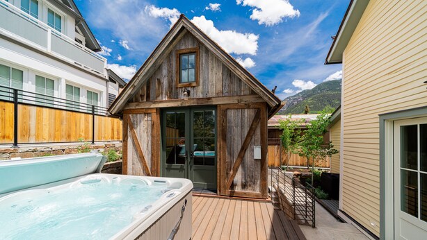 Eine Holzhütte mit Whirlpool und Terrasse, umgeben von einem Holzzaun und einem Bergpanorama.